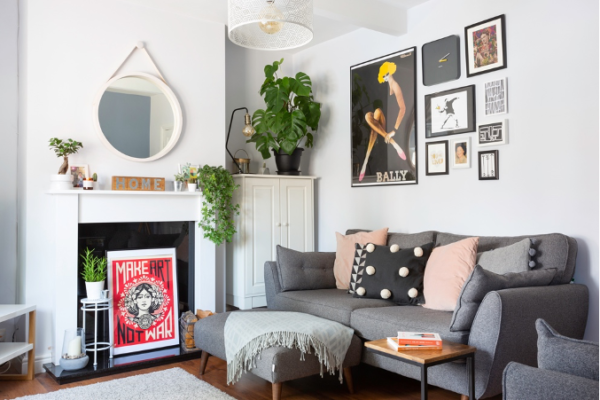 A living room with a grey sofa, houseplants, a mirror and lots of wall art on the wall